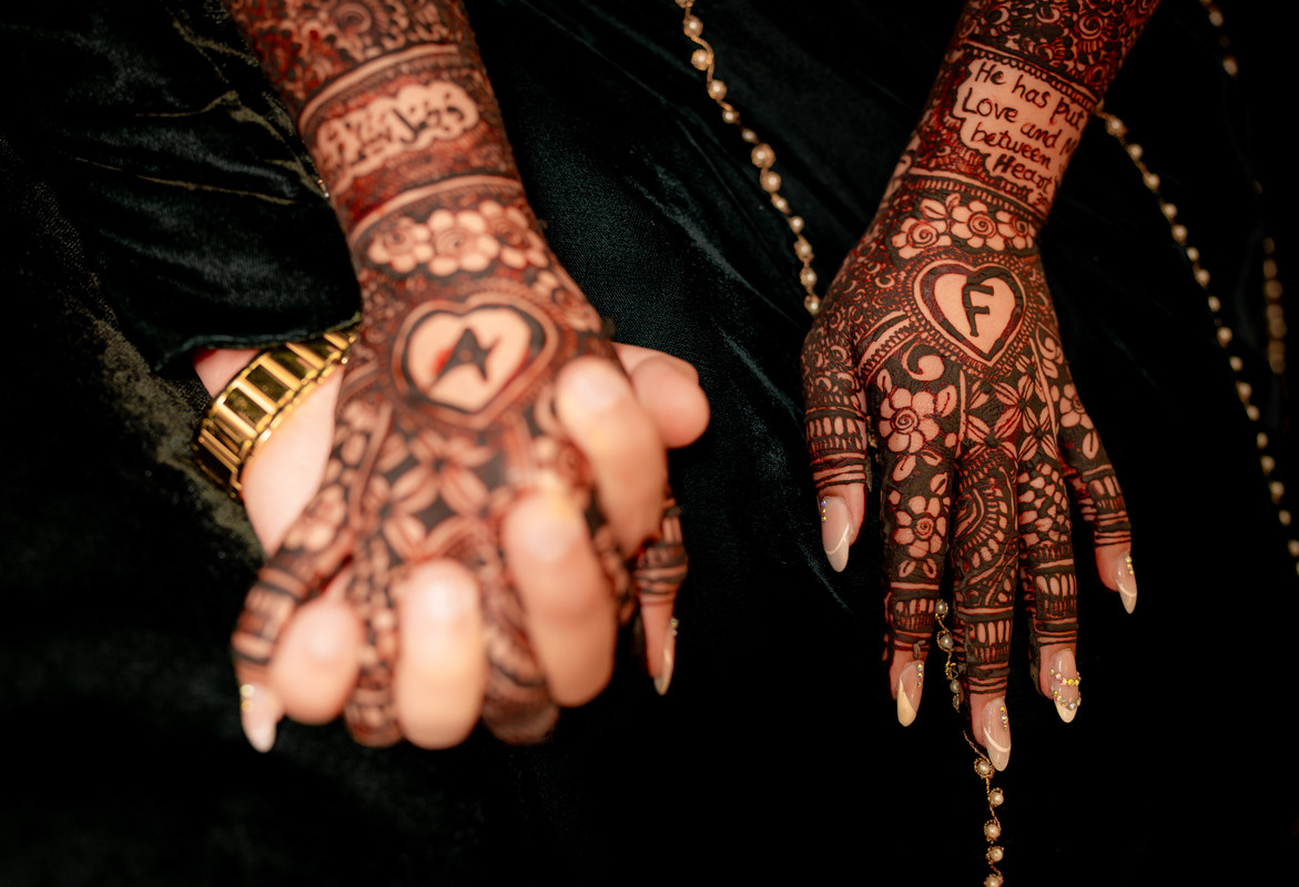 Close-up of the couple’s hennaed hands, with initials inside hearts and a love verse written in mehndi
