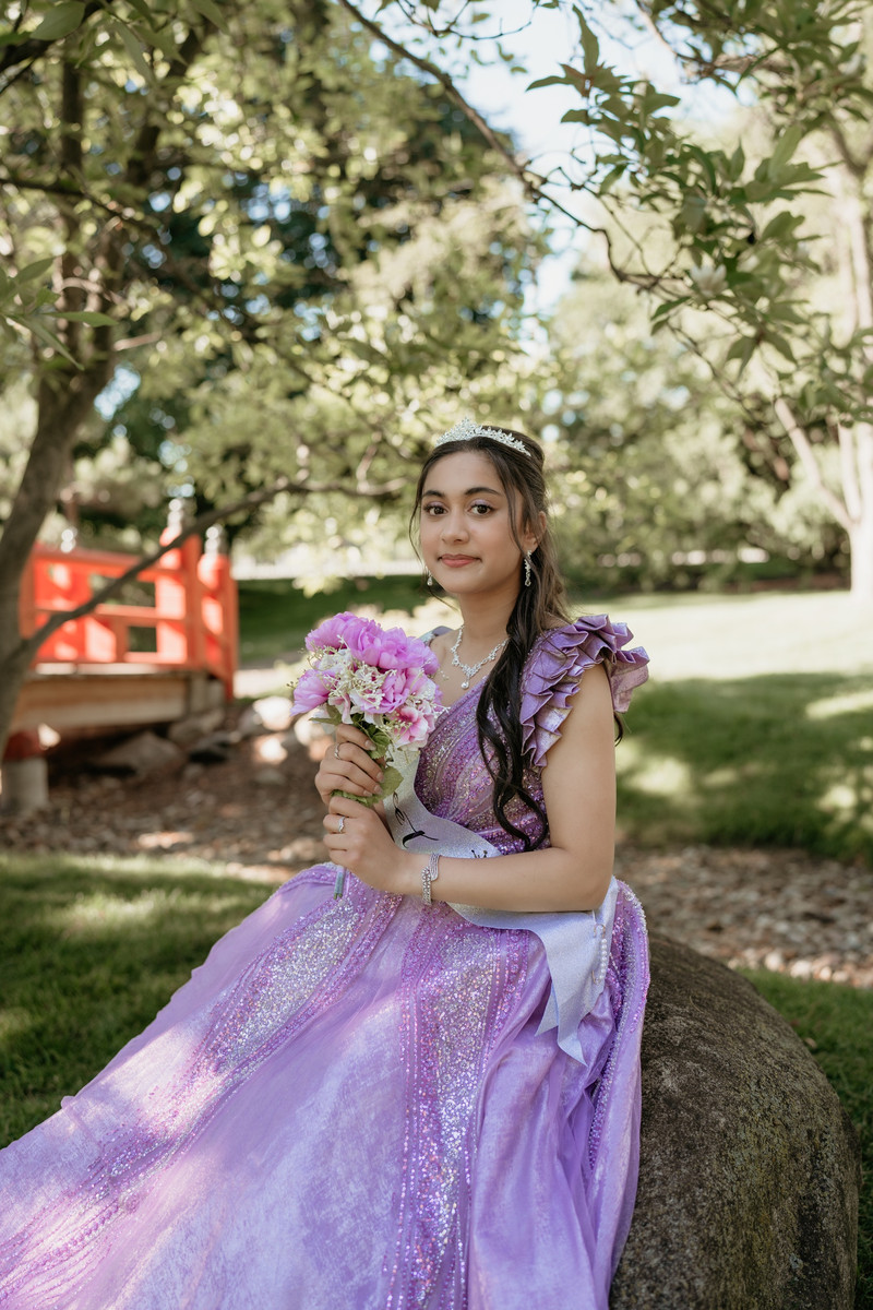 Young woman in a lavender sequined gown and tiara holding pink flowers in a garden