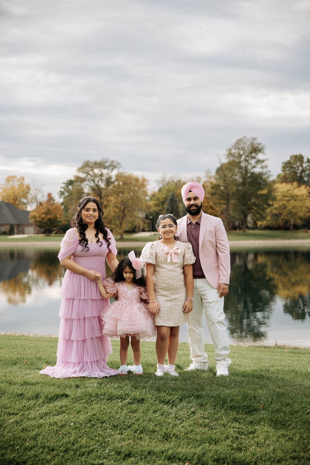 Family of four dressed in pink standing by a lake in autumn for a fifth birthday celebration
